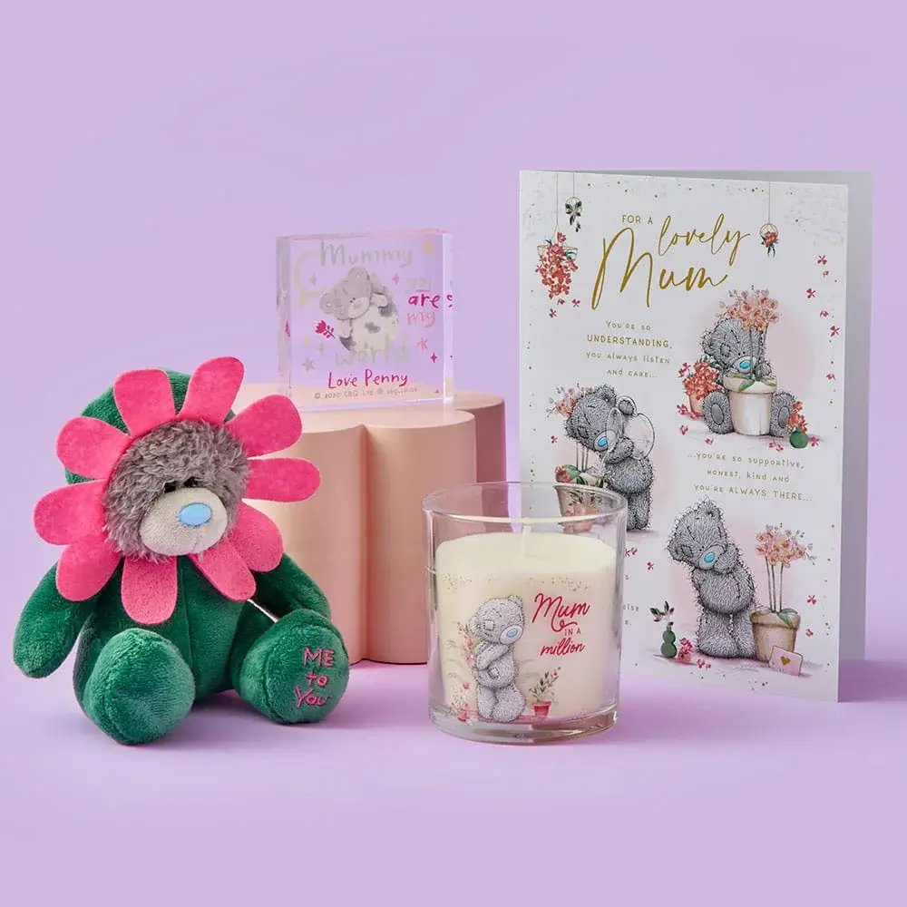 A cute Mother’s Day gift set featuring a flower‑costumed teddy bear, a scented candle with a bear illustration, a small personalised acrylic block, and a floral card, all arranged on a pastel purple background.